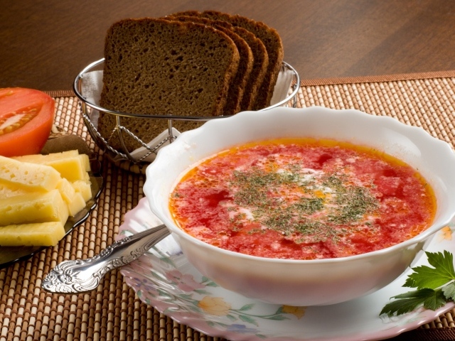 A plate of red borscht on the table with cheese and black bread