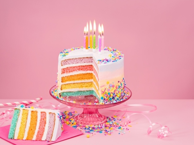Разноцветный праздничный торт со свечами на розовом фоне