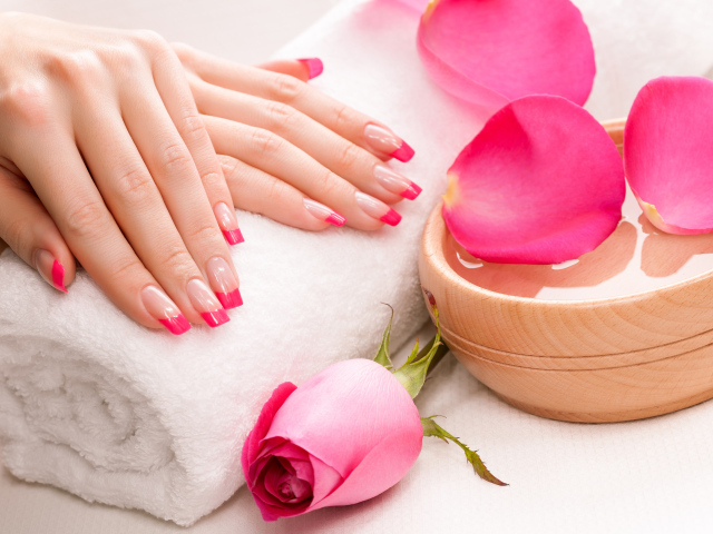 Женские руки с красивым маникюром лежат на белом полотенце на столе с розой