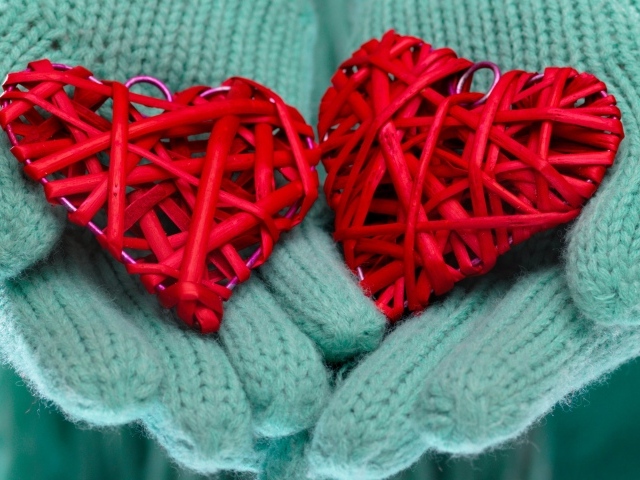 Два плетеных красных сердца лежать на руках в варежках