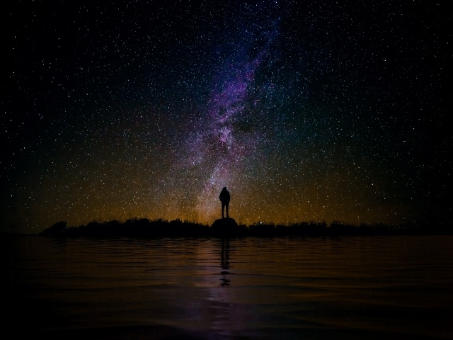 Silhouette of a man standing on a stone near the water under a starry sky