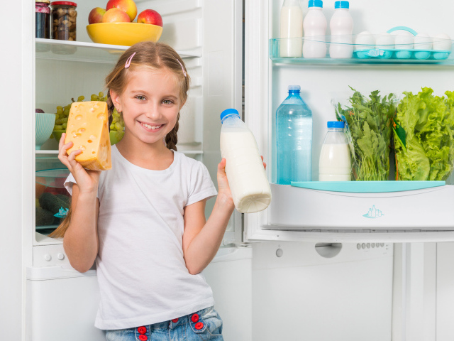 Улыбающаяся девочка у холодильника с сыром и молоком