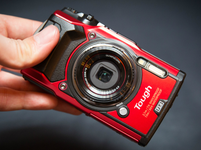 Red Olympus Tough TG-5 in hand on gray background