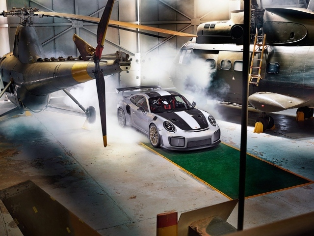 Автомобиль Porsche 911 GT2 RS в ангаре с вертолетами