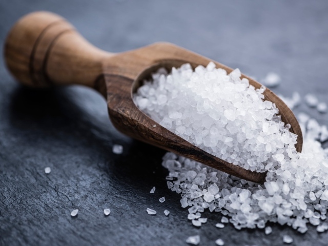 Крупная белая соль в лопатке на столе 