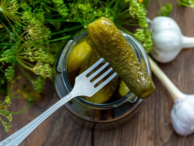 Pickled cucumbers in a jar on a table with garlic and dill