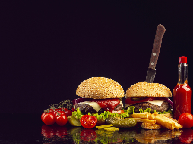 Two hamburgers on a table with a knife, vegetables and ketchup
