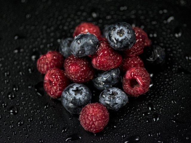 Мокрые ягоды черники и малины на черном фоне