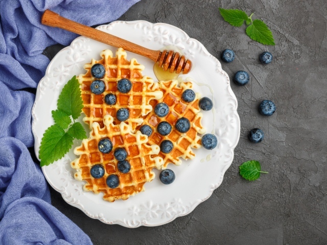 Sweet waffles with honey on a plate with blueberries