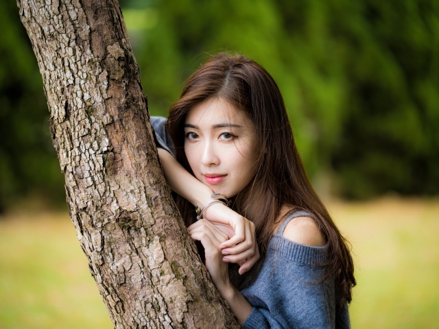 Мечтательная девушка азиатка стоит у дерева