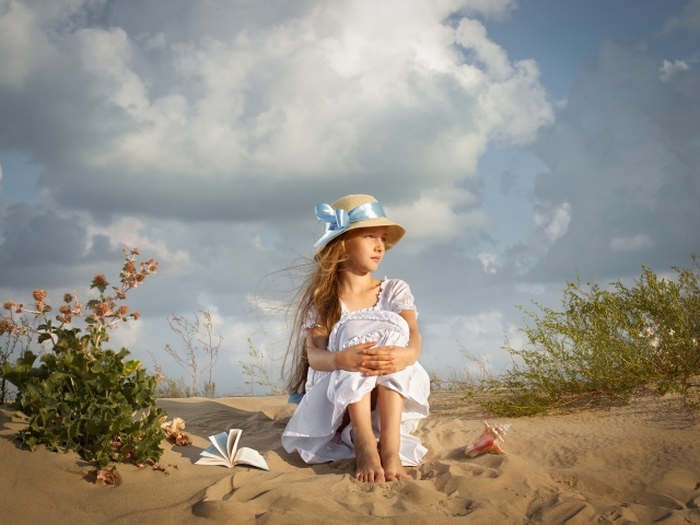 Little girl in a white dress sits on the sand