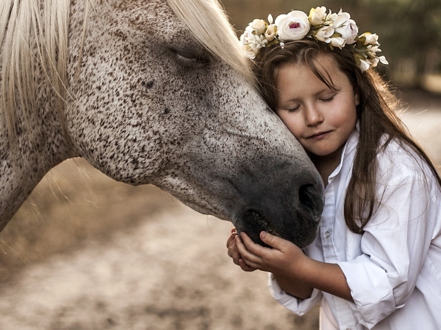 Маленькая девочка с венком на голове обнимает лошадь