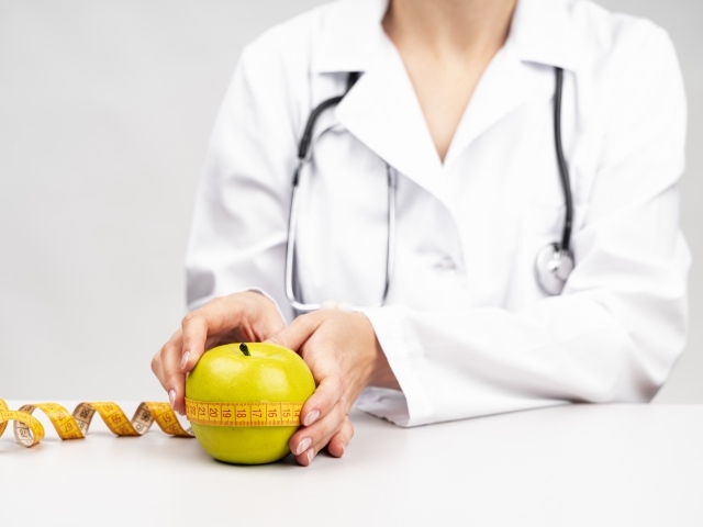 Женщина врач измеряет яблоко сантиметром 