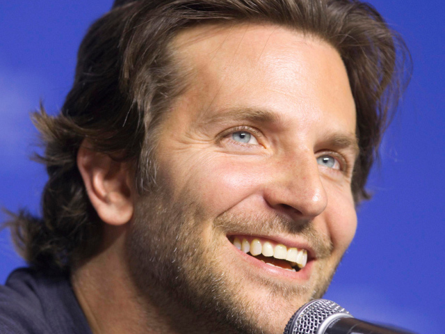 Blue-eyed actor Bradley Cooper with microphone on blue background