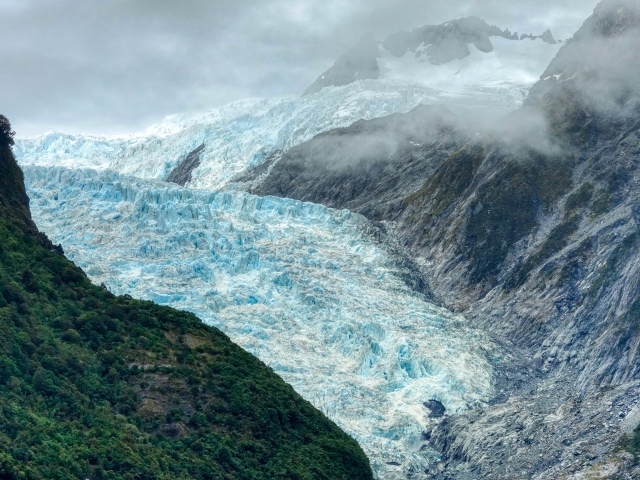 Blue glacier between rocks under stormy sky