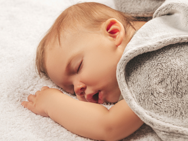 Маленький спящий ребенок под серым покрывалом 