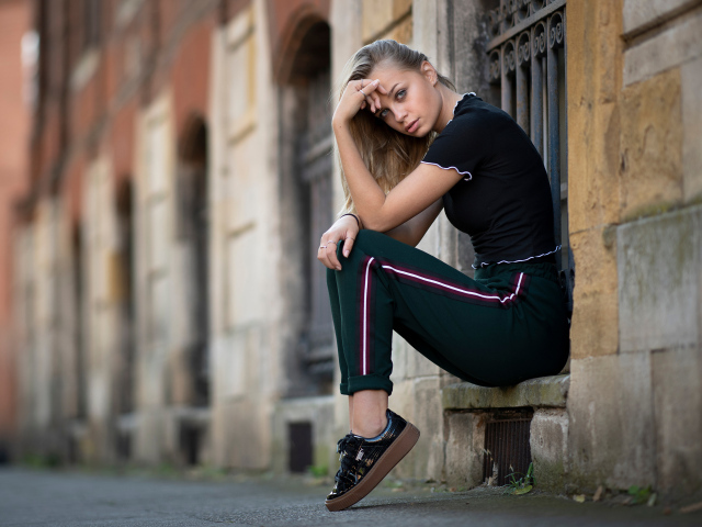 A girl in a tracksuit sits in front of a building