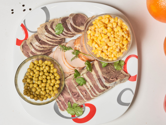 Meat products on a plate with corn and green peas