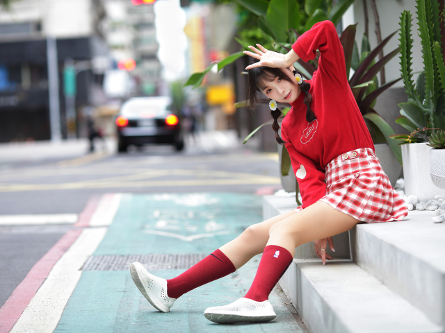 Веселая девушка азиатка в красном костюме сидит на ступеньках 