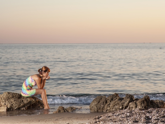 Грустная девушка сидит на камне у моря
