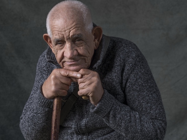 Elderly man in warm sweater on gray background