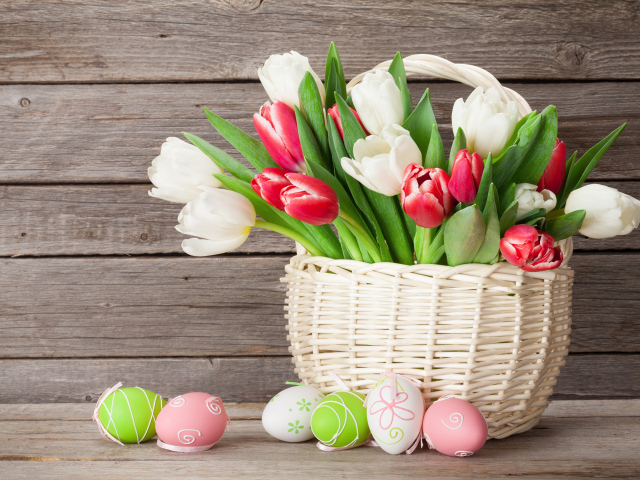 Белые и красные тюльпаны в корзине на столе с разноцветными яйцами на Пасху