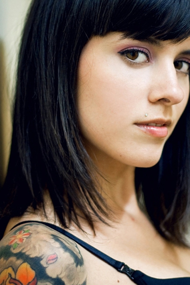 Девушка брюнетка с пирсингом в губе и татуировкой на плече