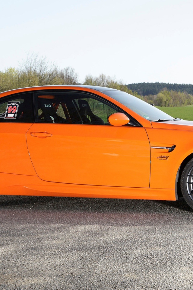 Оранжевый BMW M3 GTS на фоне зеленого поля