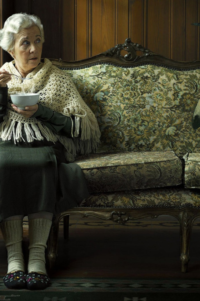 Пожилая женщина кушает суп и смотрит на пингвина