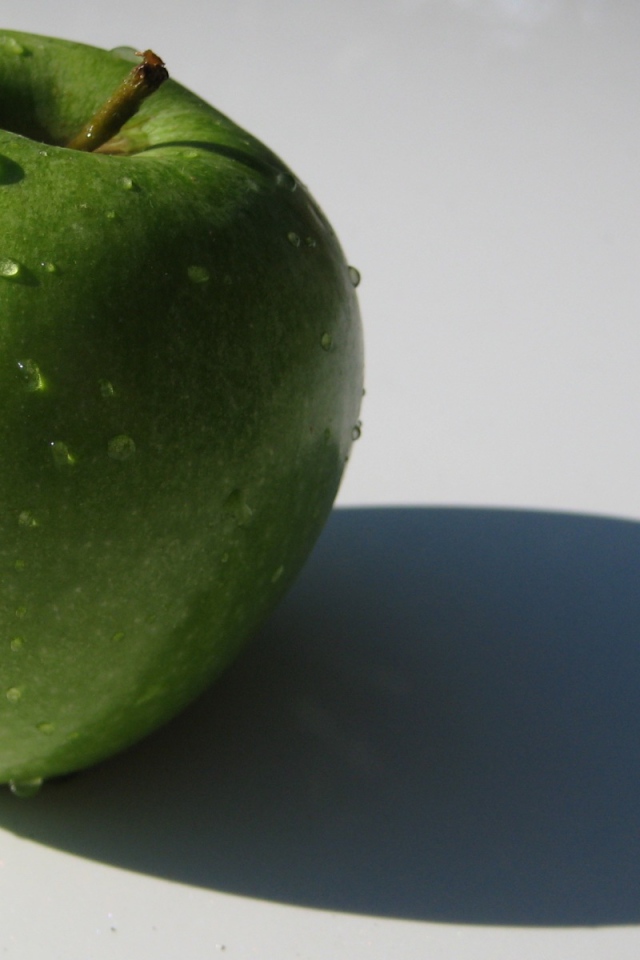 Зеленое яблоко на белой поверхности