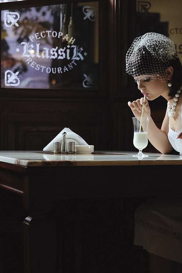 Девушка в белом платье пьет коктейль в ресторане