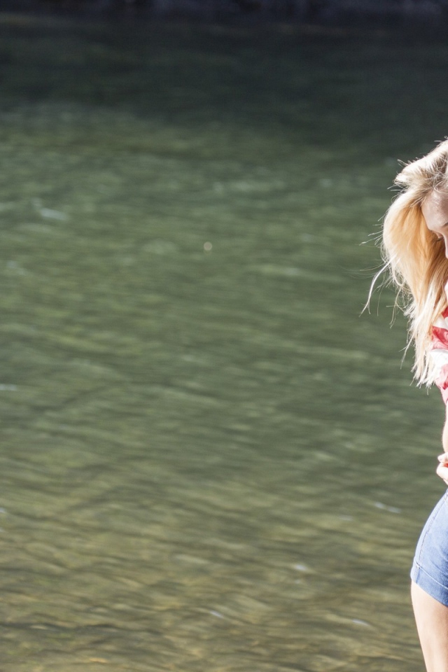 Блондинка в джинсовых шортах стоит на фоне воды