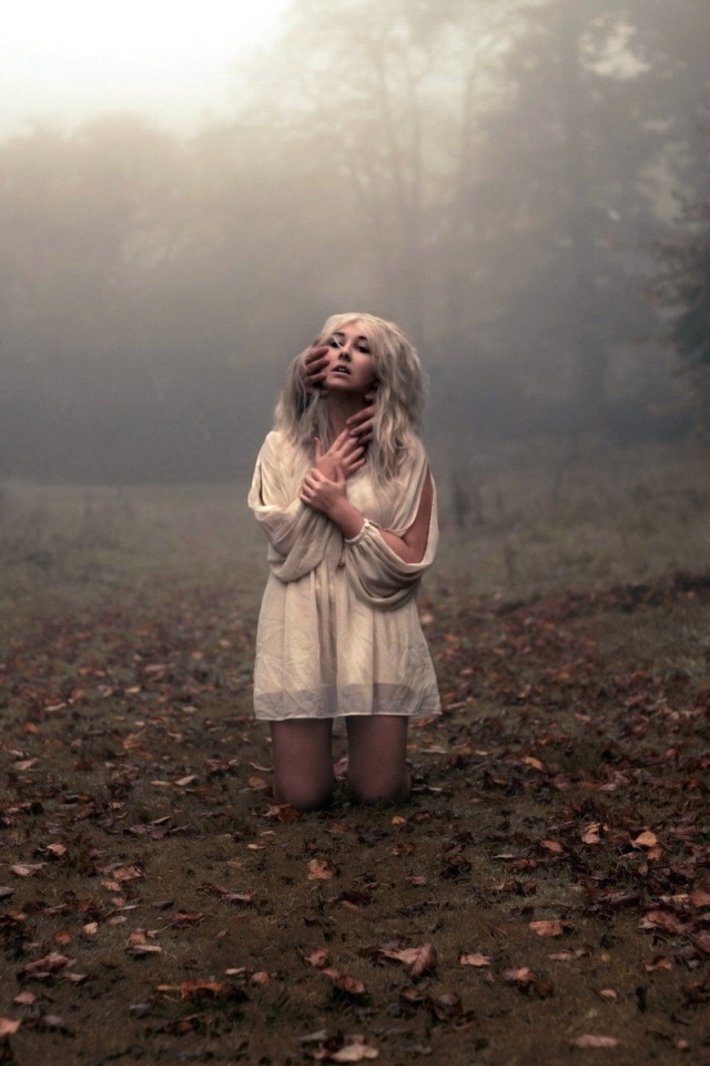 Блондинка в белом платье стоит на коленях среди леса