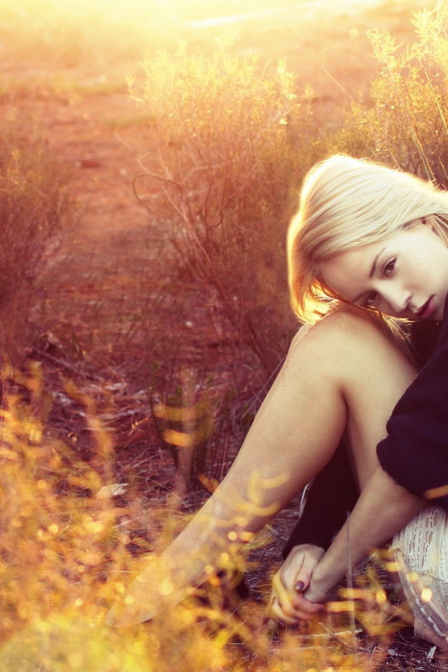 Блондинка сидит среди кустарников