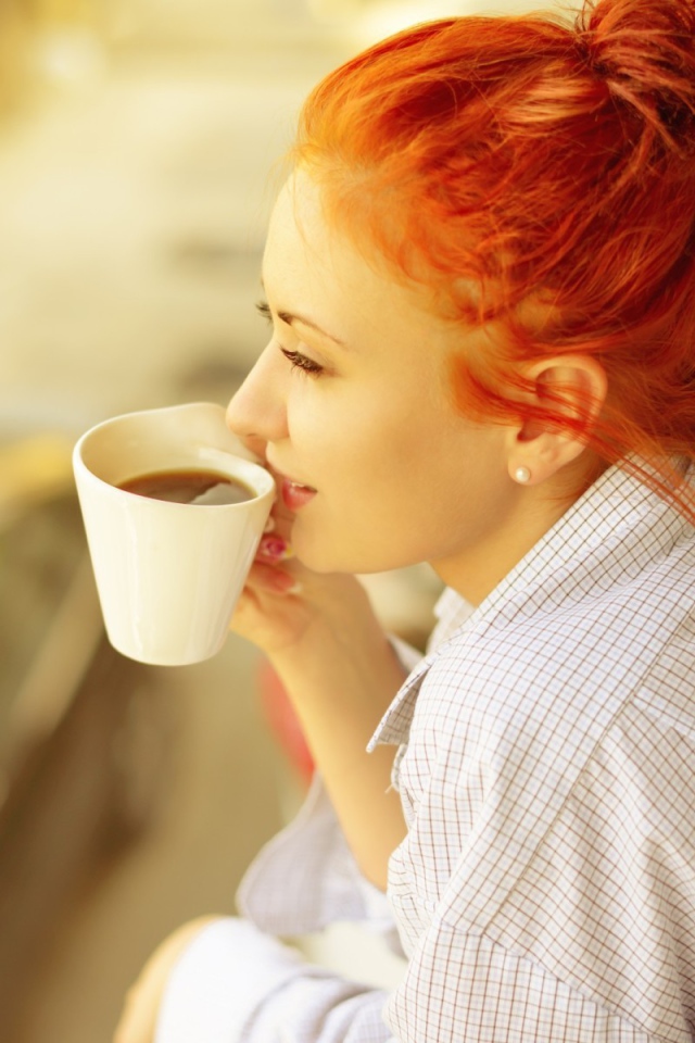 Ярко рыжая девушка в рубашке пьет кофе