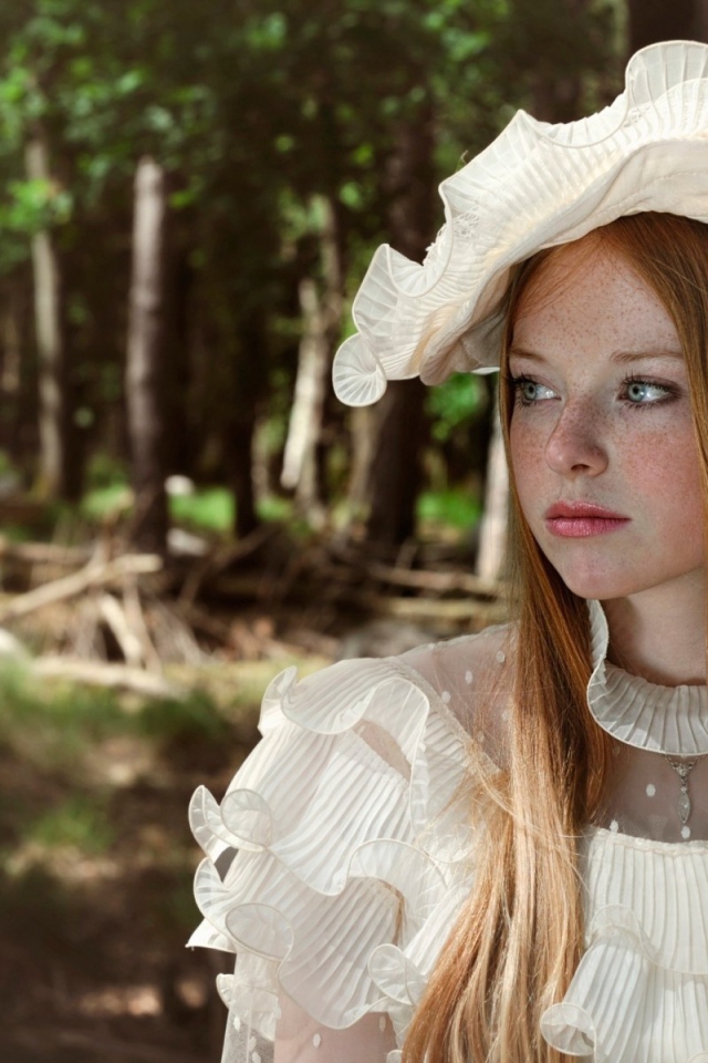 Веснушчатая девушка в белой шляпке стоит у дерева