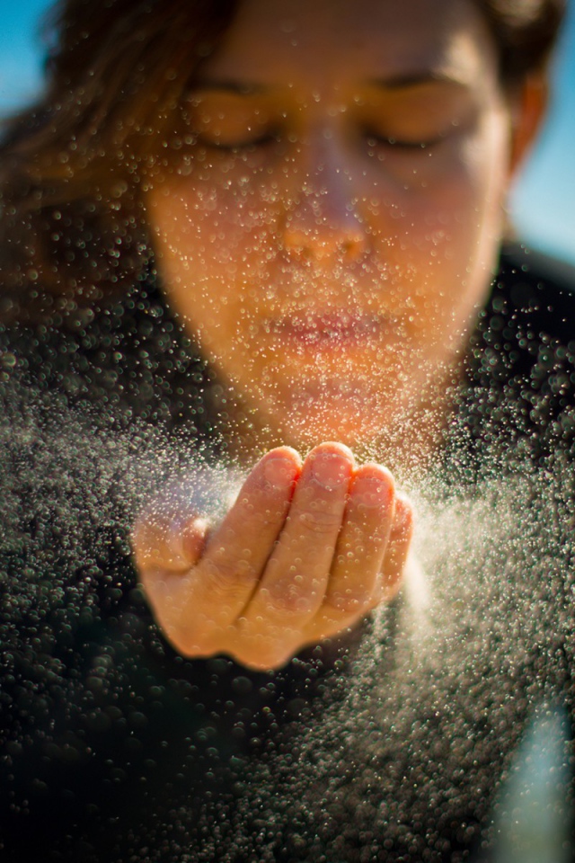 Девушка сдувает песок с руки