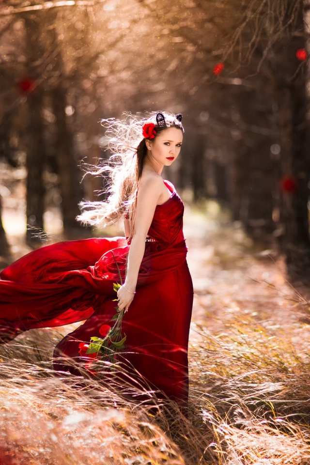 Девушка в красном платье стоит в ветренном лесу