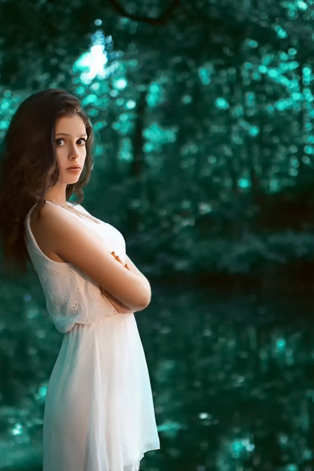 Девушка в белом платье стоит в зеленом лесу