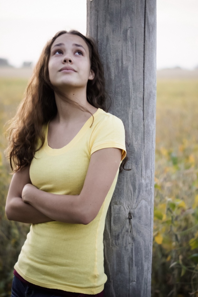 Девушка в желтой майке стоит у столба