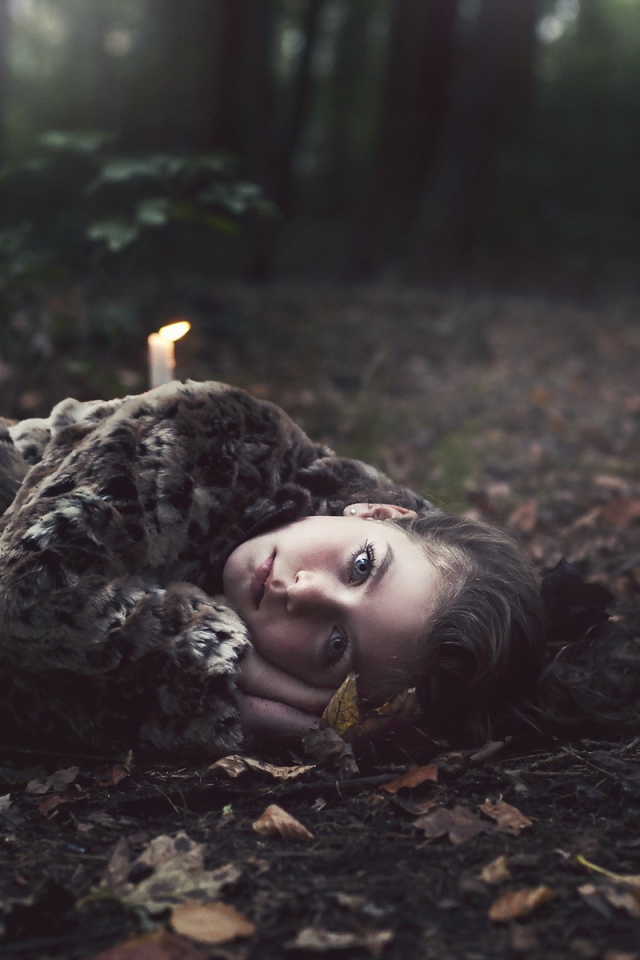 Девушка лежит среди свечей в лесу