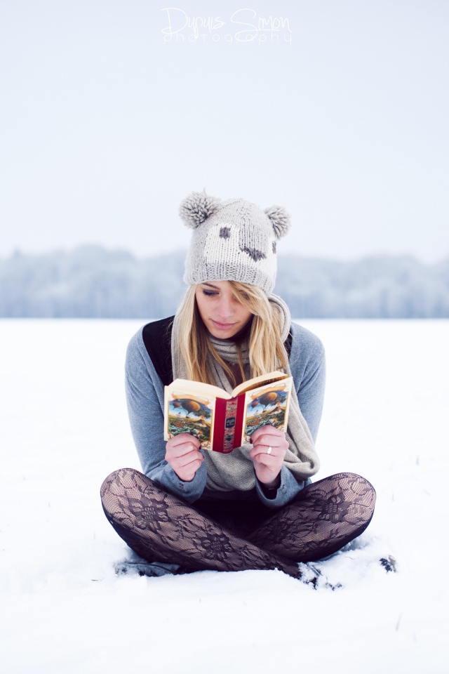 Девушка читает книгу сидя на снегу