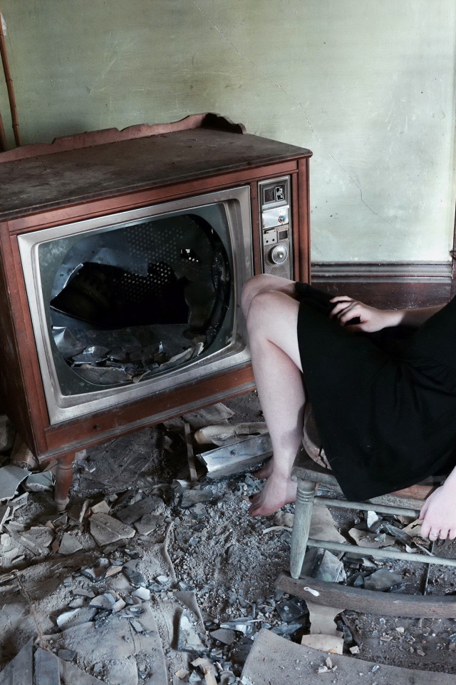 Девушка сидит у разбитого старого телевизора
