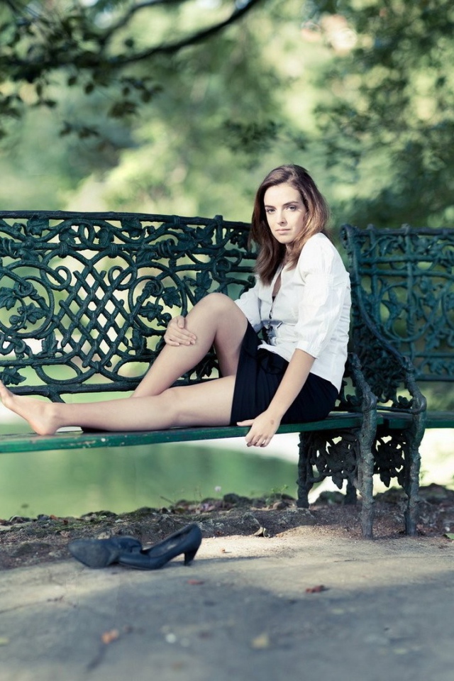 Девушка сидит на кованной парковой скамье