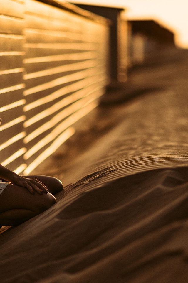 Девушка сидит на песке у забора