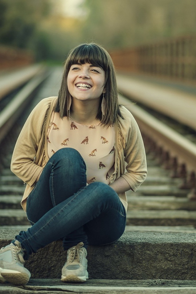 Девушка улыбается сидя на рельсах