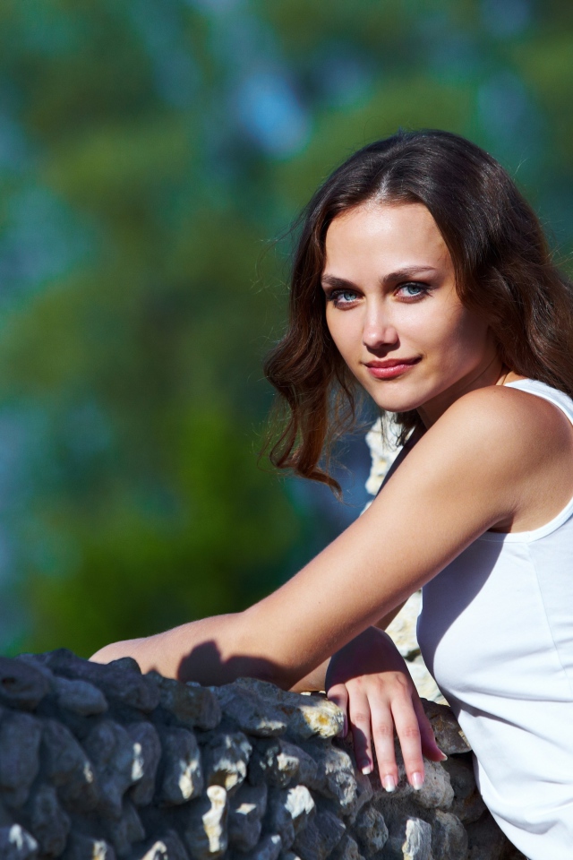 Девушка стоит у забора из камня