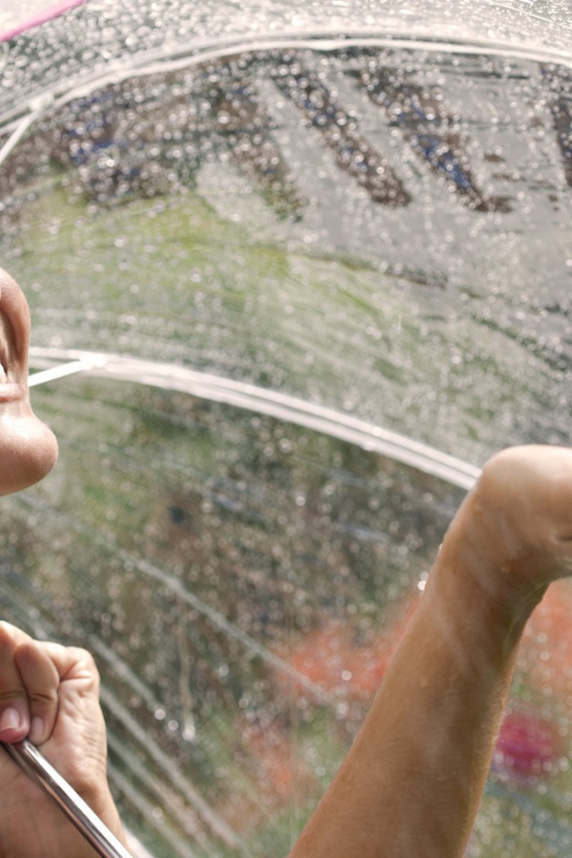 Девушка под прозрачным зонтом ловит дождь рукой