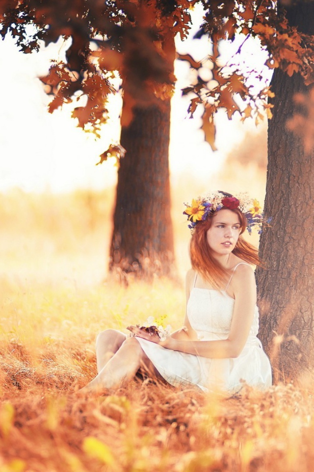 Девушка с венком на голове сидит под осенним деревом