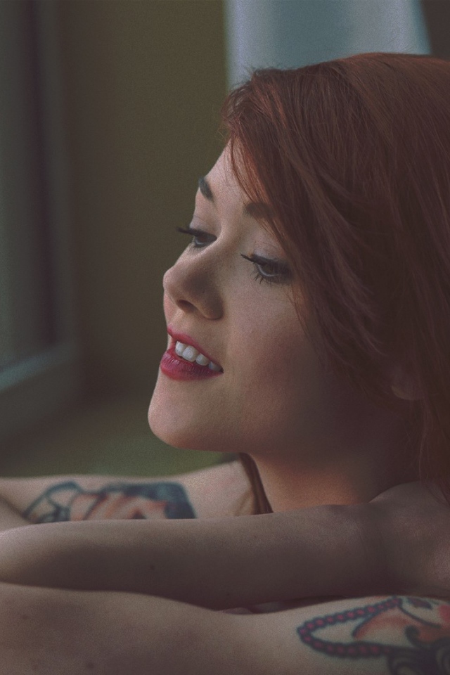 Девушка с татуировками смотрит в окно